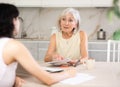 Elderly woman discussing deal with saleswoman in kitchen