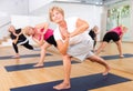 Elderly woman doing twisting asana Parivritta Parsvakonasana in yoga studio