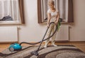 Elderly woman doing woman chores at home. Vacumming the carpet