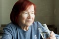 elderly woman drinking mineral water from glass. Closeup portrait of red-haired senior woman in blue jumper, quenches thirst, at Royalty Free Stock Photo