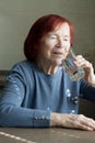 elderly woman drinking mineral water from glass. Portrait of red-haired senior woman in blue jumper, quenches thirst, sitting at Royalty Free Stock Photo