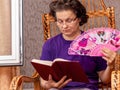 An elderly woman with a fan in her hand reads the Bible. Woman in a chair with a book by the open window Royalty Free Stock Photo