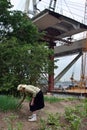 Elderly woman farmer inspects plants planted in field, over bridge