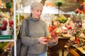 Elderly woman in festive mood choosing Christmas decorations in store Royalty Free Stock Photo