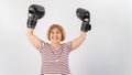 An elderly woman in fighting gloves raises her hands up on a white background. Victory in a duel