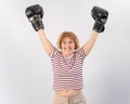 An elderly woman in fighting gloves raises her hands up on a white background. Victory in a duel