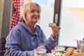 Elderly woman finds pure joy in the early morning as she savors a wholesome breakfast on the porch of her rustic cottage