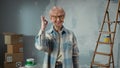 Elderly woman in glasses is looking at camera, showing ok gesture and smiling. Portrait of female pensioner in blue Royalty Free Stock Photo