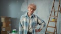 Elderly woman in glasses is looking at camera and smiling. Portrait of female pensioner in blue plaid shirt is posing in Royalty Free Stock Photo