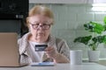 Elderly woman in glasses shopping online with credit card using laptop computer at home Royalty Free Stock Photo