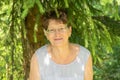 An elderly woman in glasses sits in nature and looks at the camera. The concept of old age, wisdom and joy