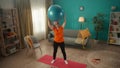 Elderly woman goes in for sports with a fitness ball in the living room. A greyhaired woman holds a ball over her head