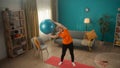 Elderly woman goes in for sports with a fitness ball in the living room. A greyhaired woman holds a ball over her head