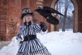 An elderly woman in a gothic dress with a black raven hat on nature in winter