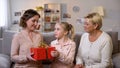 Elderly woman with granddaughter presenting gift box mother, holiday tradition