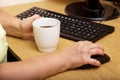 An elderly woman hand on a computer mouse. The old grandmother works behind the computer keyboard and drinks coffee Royalty Free Stock Photo