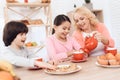 Elderly woman and happy grandson and granddaughter drink tea from red mugs in kitchen.