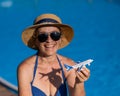 An elderly woman in a hat and sunglasses holds a model airplane while sitting by the pool. Retirement vacation concept. Royalty Free Stock Photo