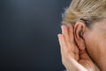 Elderly woman with hearing aid on grey background. Deafness concept.