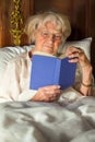 Elderly woman in her nightgown reading in bed