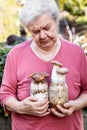 Elderly woman holding home cultivated mushrooms, selfmade fungiculture on glasses