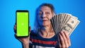 Elderly woman holding phone with green screen in one and money in another hand. Lottery win