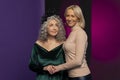 An elderly woman holds the hand of a young blonde on a colored background in the studio.  Perhaps they are a grandmother and her g Royalty Free Stock Photo