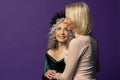 An elderly woman holds the hand of a young blonde on a colored background in the studio.  Perhaps they are a grandmother and her g Royalty Free Stock Photo