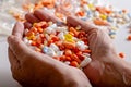 An elderly woman holds a lots of colored pills in hands on a white background.