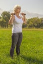 Elderly woman lifts dumbbells while doing fitness in a city park against the backdrop of mountains