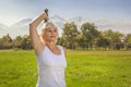 Elderly woman lifts dumbbells while doing fitness in a city park against the backdrop of mountains