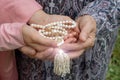 An elderly woman and a little girl are holding a beautiful white rosary. Hands of an old woman and a little girl with pearl rosary