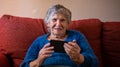 Elderly woman looking at camera while using a mobile phone sitting on sofa home Royalty Free Stock Photo