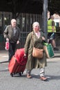 Elderly woman with luggage wearing face mask walking across street