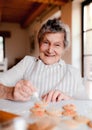 Elderly woman making and decorating cakes in a kitchen at home.