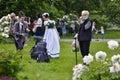 An elderly woman in a mask enjoys peony flowers in the botanical garden.