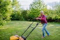 Elderly woman mowing grass with lawn mower in the garden, garden work concept. Royalty Free Stock Photo