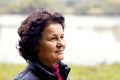 An elderly woman in nature with a slight smile feels happy. Portrait of an elderly woman looking up near the river on a blurred