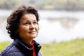 An elderly woman in nature with a slight smile feels happy. Portrait of an elderly woman looking up near the river on a blurred