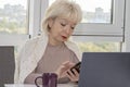 An elderly woman in the office is working on a laptop and making a call on her mobile phone, beautiful view from the window Royalty Free Stock Photo