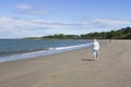 An elderly woman and others walk the beach for exercise