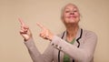 An elderly woman points her finger to attract attention on a beige background