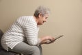 Elderly woman with poor posture using tablet on beige background