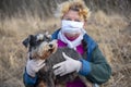 An elderly woman in a protective medical mask and rubber gloves on a walk with a dog