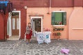 Elderly woman puts her washing on a drying rack in front of her colorful house in Burano, Venice, Italy Royalty Free Stock Photo