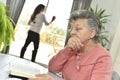 Elderly woman reading a book with a home carer in the background