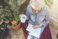 Elderly woman reads book surrounded by plants with cup in her hand Royalty Free Stock Photo