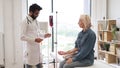 Elderly woman receiving blood transfusion looking at medical doctor.