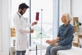 Elderly woman receiving blood transfusion looking at medical doctor.