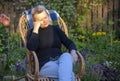 An elderly woman rests in a wicker chair in her garden.